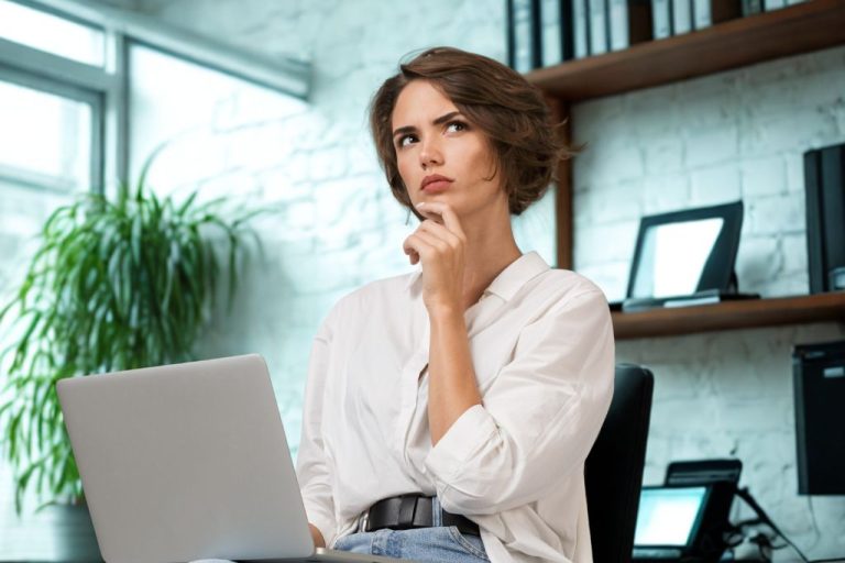 A weboldal ujratervezés gondolatán tűnődő hölgy, ül a számítógép előtt egy irodában.